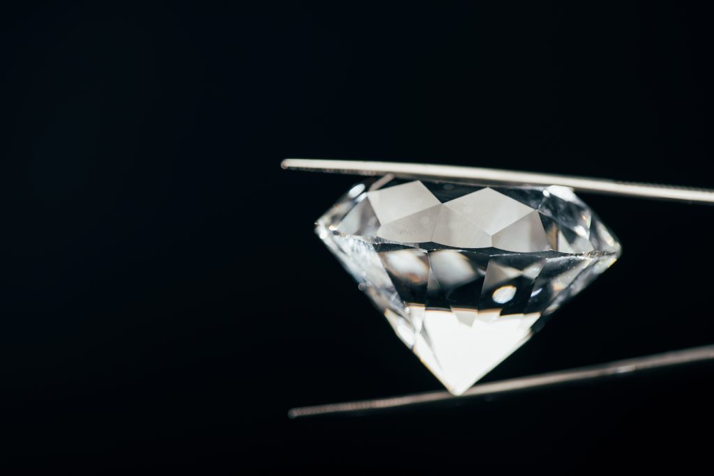 Diamant von der Seite gehalten mit Pinzette vor schwarzem Hintergrund