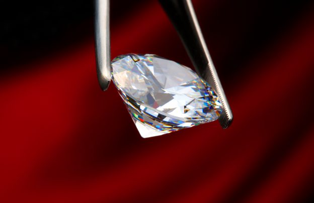 Diamant der von Pinzette gehalten wird vor rotem hintergrund